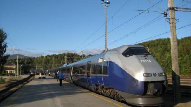 Dombås stasjon, tog til Åndalsnes i bakgrunnen (Raumabanen), tog fra Trondheim til Oslo i forgrunnen (Dovrebanen) (Fotograf: Dagmar Buen © Fylkesarkivet i Oppland) Bilde tog Dombås stasjon