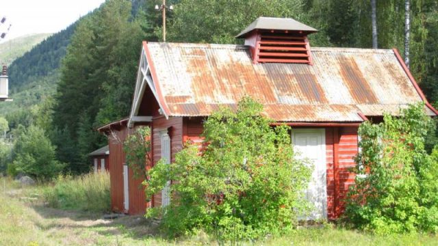 Sjoa stasjon, privetet (utedoen) fotografert fra stasjonsbygningen. NB! Porselensskålene for strømledninger på taket. (Fotograf: Dagmar Buen © Fylkesarkivet i Oppland). Bilde av utedoen ved Sjoa stasjon