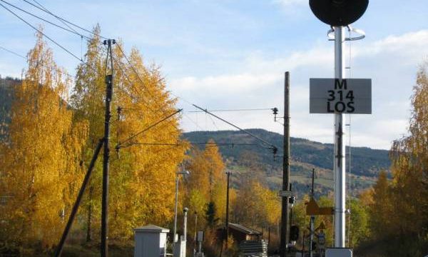 Losna stasjon, planovergangen med lagerbygningen i bakgrunnen. (Fotograf: Dagmar Buen © Fylkesarkivet i Oppland). Bilde av planovergang ved Losna stasjon
