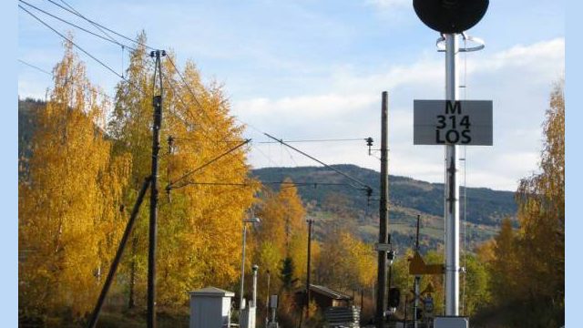 Losna stasjon, planovergangen med lagerbygningen i bakgrunnen. (Fotograf: Dagmar Buen © Fylkesarkivet i Oppland). Bilde av planovergang ved Losna stasjon