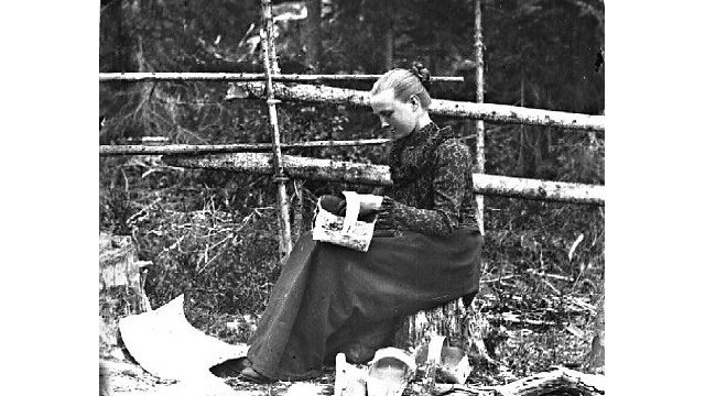 Håndarbeid. En viktig biinntekt for husmannsfamilien var produkter de lagde for salg. Jenta på bildet fletter kurver av never. – Fotograf: Lars Bleken, Foto: Randsfjordmuseene AS Sittende kvinne som fletter kurver