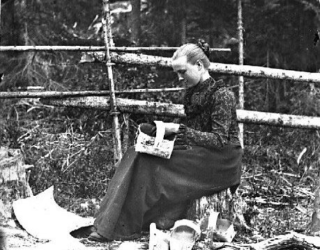 Håndarbeid. En viktig biinntekt for husmannsfamilien var produkter de lagde for salg. Jenta på bildet fletter kurver av never. – Fotograf: Lars Bleken, Foto: Randsfjordmuseene AS Sittende kvinne som fletter kurver