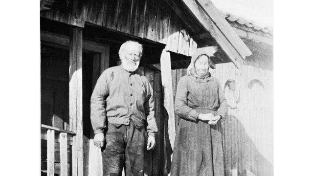 Erik og Karen på plassen Bjøraltbråten i Lunner, 1930 – Foto: Randsfjordmuseene AS Eldre mann og kvinne foran hus