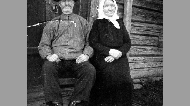 Husmannsfolk i Korsvollhagen, 1925 - Kristian Mathiassen Korsvollhagen (f. 1865) og kona Inge Maria Kristiansdatter (f. 1861), fotografert foran stua på plassen Korsvollhagen under Aslakrud i Kolbu ca. 1925. Inge Maria var da blitt blind. På husmannsplassen hadde de ei ku, en gris og noen høner, og ca. fem mål jord. – Fotograf: Ukjent. Foto: Mjøsmuseet / R 79/025/06. Sittende eldre mann og kvinne