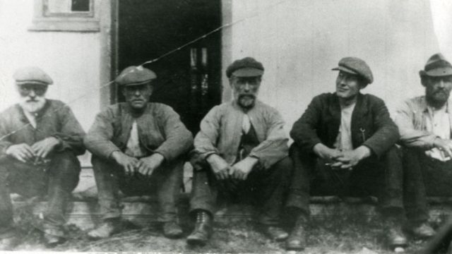 Husmenn under Kompelien – Foto: Randsfjordmuseene AS Fem menn som sitter på en trapp utenfor en bygning