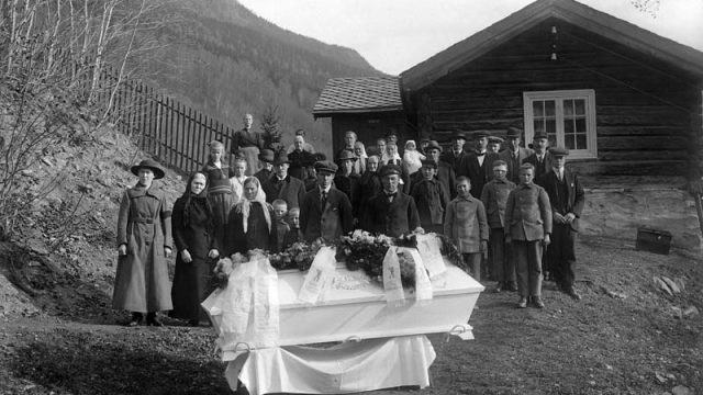 Begravelse - Før den siste ferden. – (Foto: Hans H. Lie, Maihaugen - SS-HHL-24594) Stor gruppe mennesker står bak en kiste i en utendørs begravelse