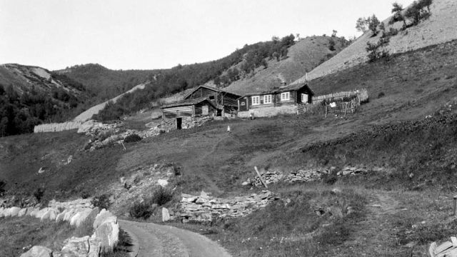 Plassen Skulemesterstugu i Vågå fotografert ca. 1930. – (Foto: Hans Joramo, Maihaugen - SS-HJM-0023) Vei i forgrunnen med sidevei opp til en gårdsplass i bakgrunnen i en bakke