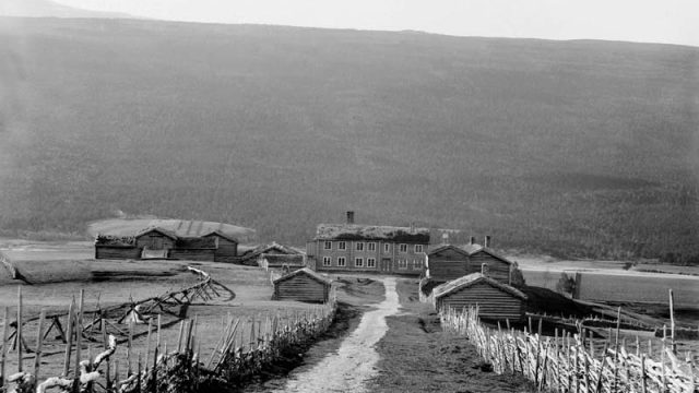 Lesja prestegård fotografert ca. 1895. En av husmennene under prestegården var pålagt vedlikehold av vannledningen til høyre på bildet. – (Foto: Mathias P. Lien, Maihaugen - SS-MPL-0067) Utsikt til en større bygning med flere bygg rundt seg
