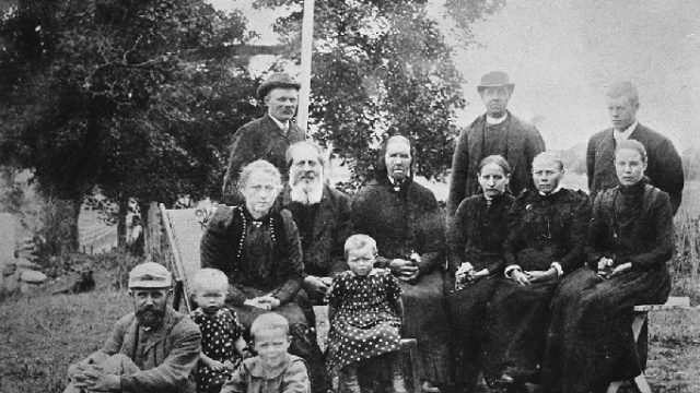 Unge husmannsfolk gifter seg, 1894 - Sittende foran: Haaken Skramstad. Barn: Johanne, Nils og Karen Skramstad. Sittende: Anna Skramstad, Ole og Marte Maulbørsbakken, Marte Petersborg, bruden Malla, N.N. (søster til Even Myrsveen). Stående: Julius Petersborg, Nils Kraby og brudgommen Even Myrsveen. Foto tatt på Skramstad 1894. – Fotograf: Ludvig Christensen. Foto: Mjøsmuseet / R 78/003/14. Ti voksne og tre barn poserer foran kamera